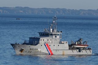 Patrouilleur des douanes avec le drapeau français peint sur sa coque, en mer, à proximité d'une côte