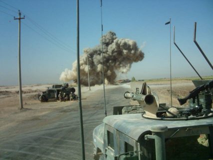 Deux véhicules légers de l'armée américaine. Au loin, un nuage de fumée provoqué par un tir de roquette.
