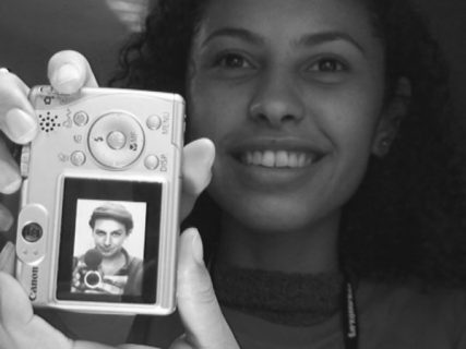 Le portrait d'une jeune fille tenant dans ses mains un appareil photo. Sur l'écran de l'appareil, le portrait d'un homme tenant lui-même un appareil photo.