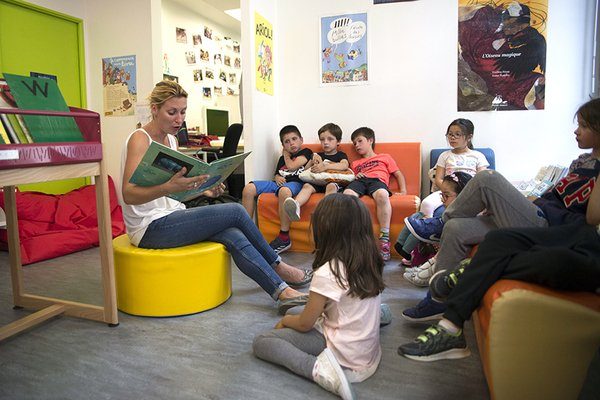 Photo d'une lectrice et d'un groupe d'enfants en bibliothèque.
