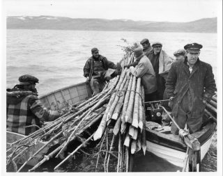 Des hommes sur une grande barque, transportant de grands bâtons.