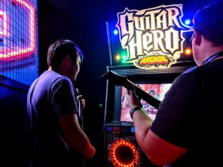Deux hommes jouent à Guitar Hero dans une salle d'arcade.